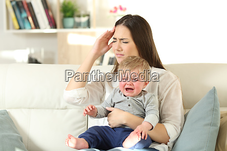 Mother suffering and baby crying desperately sitting on a couch in the living room at home
