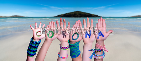 Children Hands Building Colorful English Word Corona. Ocean And Beach As Background