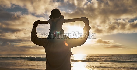 Love,  girl and father relax on beach during sunset summer vacation in Hawaii with silhouette,  clouds and water background. Man carrying child with ocean or sea view on family vacation in nature.