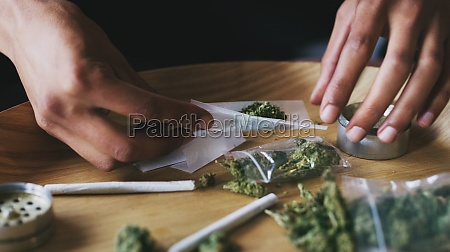 Living on the green side of life. a man rolling a marijuana joint at home